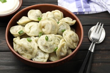 Tasty dumplings with green onion, dill and cutlery on wooden table, closeup