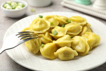 Tasty dumplings with green onion and fork on grey textured table, closeup
