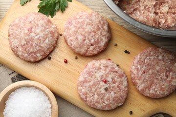 Many uncooked patties and spices on wooden table, flat lay