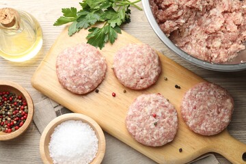 Many uncooked patties and spices on wooden table, flat lay