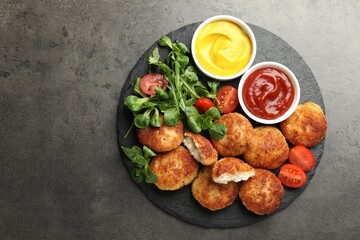 Tasty patties, tomato, spinach, mustard and ketchup on grey textured table, top view. Space for text