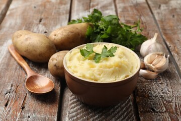 Delicious mashed potato with parsley, garlic and spoon on wooden table, closeup