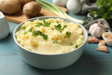 Delicious mashed potato with green onions served on light blue wooden table, closeup