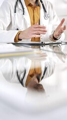 Unknown male doctor wearing a stethoscope, yellow shirt under a lab coat is gesturing with hands overs a glass desk with a laptop in clinic office. Medicine concept