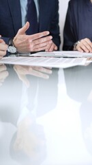 Business people are discussing a contract during meeting while sitting at the glass table in office, vertical close up view. Concept of success and team work