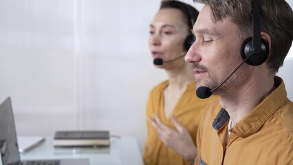 Focused male call center operator in yellow casual shirt is assisting clients online, providing customer support and answering inquiries. Call center operators