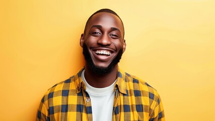 Portrait of a cheerful man in a plaid shirt smiling brightly against a vibrant yellow background, exuding positivity and confidence.
