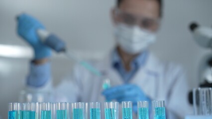 Laboratory tubes are in focus, closeup view. Female scientist researcher is using a micropipette at...