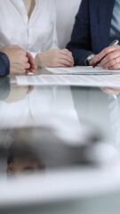 Unrecognizable business people are reviewing contract terms during a meeting while sitting at the glass table in office, vertical close up view. Copy space area