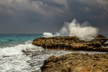 Winter storm waves crash against Ayia Napa coastline, Cyprus. Turquoise explosions contrast leaden January skies. Mediterranean raw power.