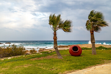 Palm trees and decorative amphora in a strong wind on the beach in stormy weather. January. ...
