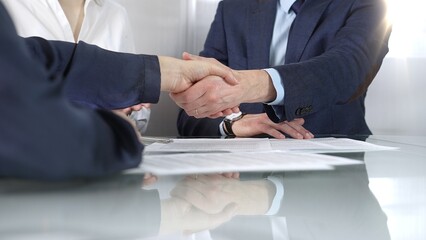 Unrecognizable business partners shaking hands after signing contract at glass table in office...