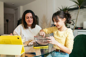 Mom and daughter baking chocolate cookies together at home, following online recipe