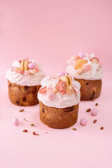 Traditional Ukrainian easter bread or sweet paska bread with topping and decorated with meringue, macarons and eggs isolated on pink background 
