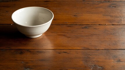 A small white ceramic bowl rests centrally on a weathered wooden table, bathed in soft natural light, creating a serene and simple atmosphere