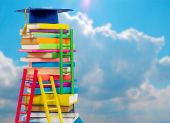 Stack of colorful books in multi-colored covers with elementary graduate cap on top against the...