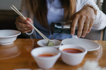Close-up of a woman pouring soy sauce on wasabi at a Japanese restaurant. Traditional Asian dining experience with chopsticks and dipping sauces. Perfect for food, culture, and culinary themes.