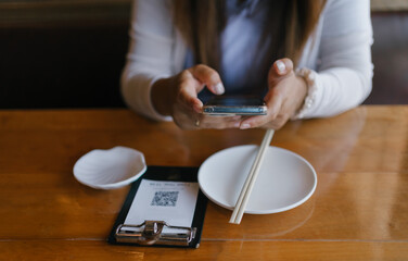 Digital dining experience. A woman uses her smartphone to scan a QR code for contactless ordering at a restaurant. Modern technology enhances convenience in cashless payments and food services.