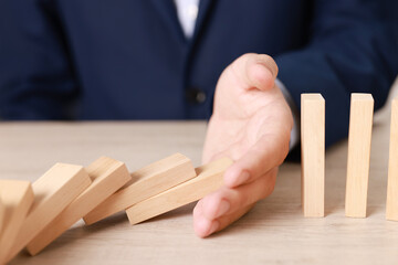 Man stopping wooden blocks from falling at table, closeup. Domino effect