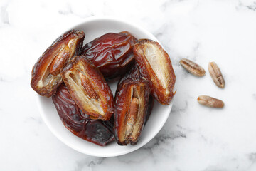 Many tasty dried dates with seeds in bowl on white marble table, top view