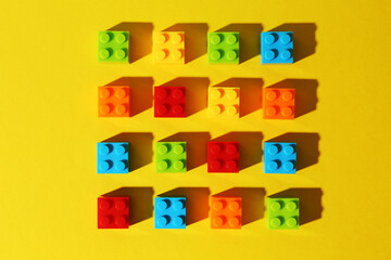 Construction toy. Colorful building bricks on yellow background, flat lay
