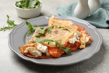 Delicious crepes with salmon, cream cheese and arugula on grey table, closeup
