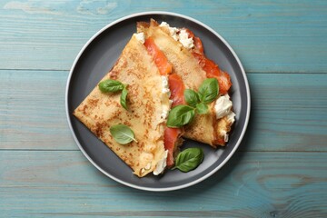 Delicious crepes with salmon, cream cheese and basil on light blue wooden table, top view