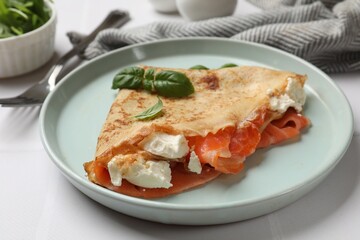 Delicious crepe with salmon, cream cheese and basil on white table, closeup