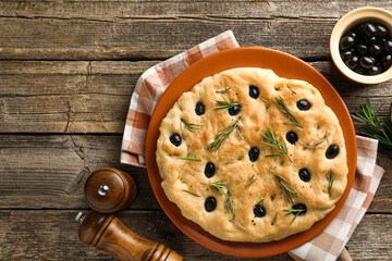 Delicious focaccia bread with olives, rosemary and spices on wooden table, flat lay. Space for text