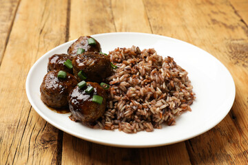 Tasty meatballs with sauce and brown rice on wooden table, closeup
