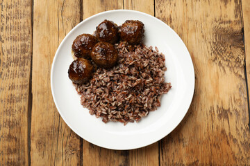 Tasty meatballs with sauce and brown rice on wooden table, top view