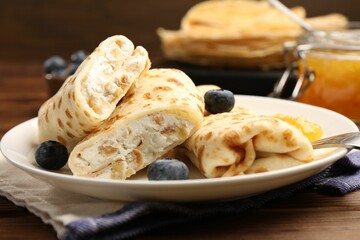 Delicious crepes with cottage cheese, jam and blueberries served on wooden table, closeup