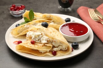 Delicious crepes with cottage cheese, jam, redcurrants and blueberries served on grey table, closeup