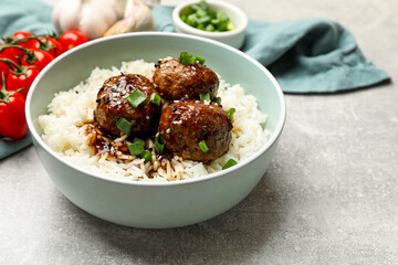 Delicious rice with meatballs, sauce and green onions on grey table, closeup