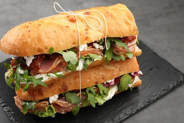 Halves of baguette sandwich with prosciutto and sun dried tomatoes on grey table, closeup