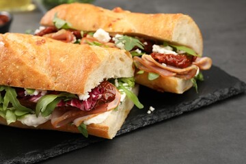 Halves of baguette sandwich with prosciutto and sun dried tomatoes on grey table, closeup