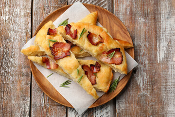 Slices of delicious focaccia bread with bacon and rosemary on wooden table, top view