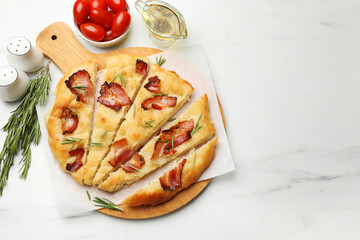 Slices of delicious focaccia bread with bacon, rosemary, oil and tomatoes on white marble table, flat lay. Space for text