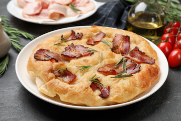 Delicious focaccia bread with bacon, rosemary, oil and tomatoes on black table, closeup
