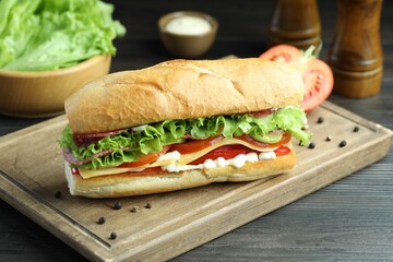 Delicious baguette sandwich with salami and cheese on grey wooden table, closeup