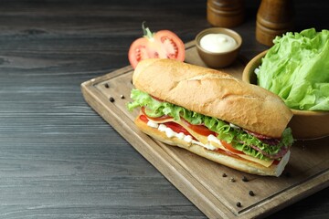 Delicious baguette sandwich with salami and cheese on grey wooden table. Space for text