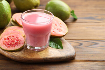 Tasty guava juice in glass, leaf and fruits on wooden table, closeup. Space for text
