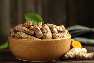 Tumeric rhizomes with leaf in bowl on wooden table, closeup