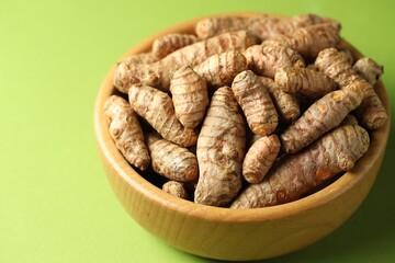 Tumeric rhizomes in bowl on green background, closeup