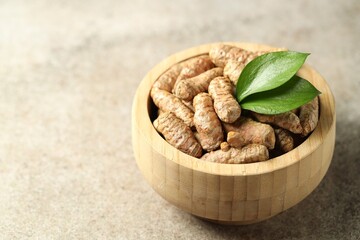 Tumeric rhizomes with leaves in bowl on grey table, closeup. Space for text