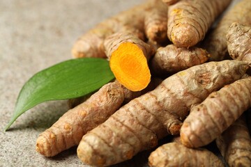 Pile of tumeric rhizomes with leaf on grey table, closeup