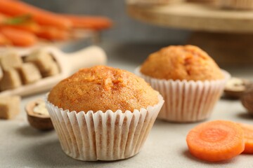 Tasty carrot muffins and cut vegetable on light grey table, closeup