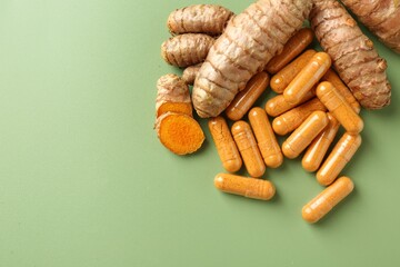 Turmeric rhizomes and capsules on green background, flat lay. Space for text