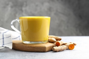 Tasty turmeric latte in cup and roots on grey table, closeup. Space for text