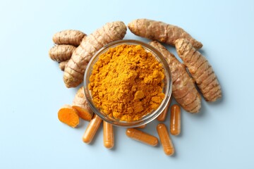 Turmeric capsules, powder and roots on light blue background, flat lay